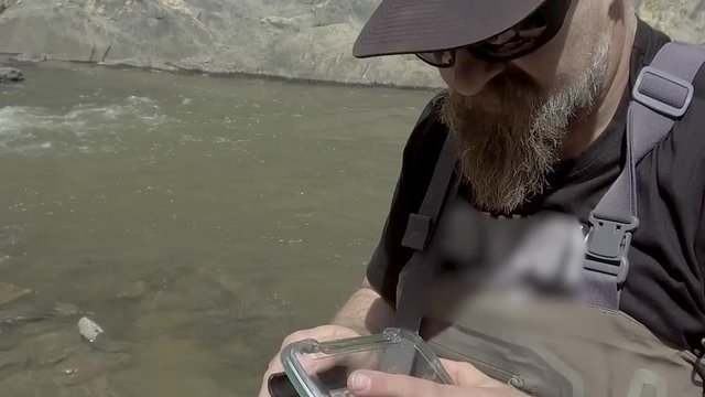 A fly fisherman selects a fly from his pack.