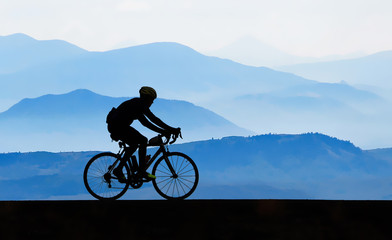 Fototapeta na wymiar Cyclist silhouetted against misty mountains.