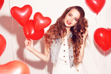 Valentine Beauty girl with red air balloons laughing, on white background. Beautiful Happy Young woman. Womans day. Holiday party. Joyful model posing, having fun, smile, celebrating Valentine's Day.