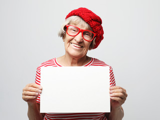 Portrait of happy senior woman with blank advertising board or copy space, over light grey...