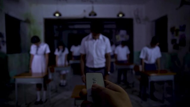 A man pressed the button on remote control then boys and girls suddenly look up and put their right hands up.