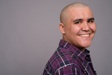 Young bald Asian businessman against gray background