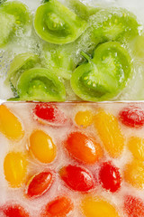 Fresh red, yellow tomatoes and green tomato slices frozen in ice cube on white background. Studio shot.