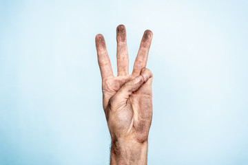 Male dirty hand showing three fingers on blue background