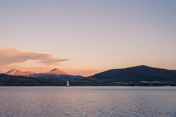 Lonely mountain lake with sailboat and alpenglow on peaks after sunset in blue hour