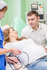 Obraz premium Nurse measuring pressure of pregnant woman. Husband supports pregnant wife for examination