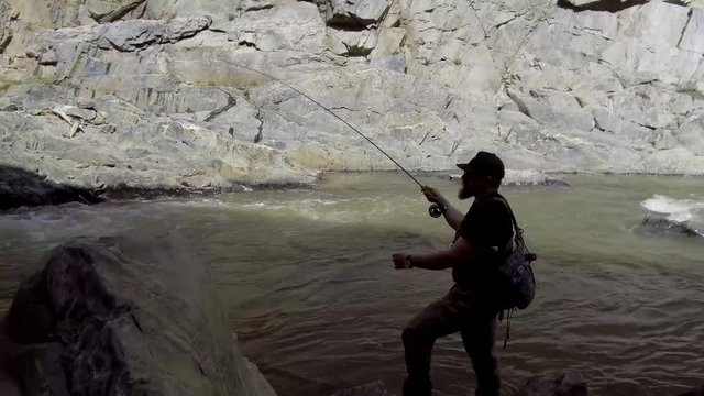 A fly fisherman is silhouetted while casting and mending upstream in a roaring river.