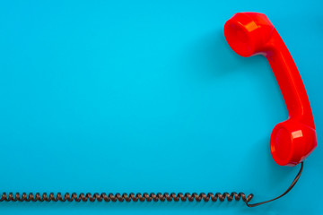 Contact us concept with a vintage red telephone handset next to the curly phone cable isolated on blue background with copy space