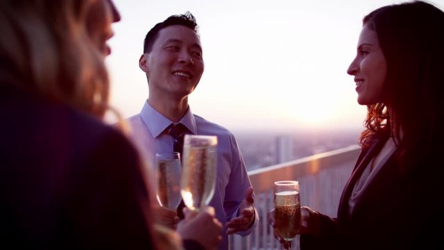 Group of multi ethnic managers toasting with champagne on rooftop at sunset
