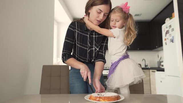 The mother tries to cut the pie. The baby hugs her and tells her a funny story. After the mother laughs, smiles and holds her daughter.