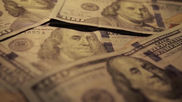Panning shot of hundred-dollar bills, slowly becomes brighter.  Close up featuring bills covering entire frame.