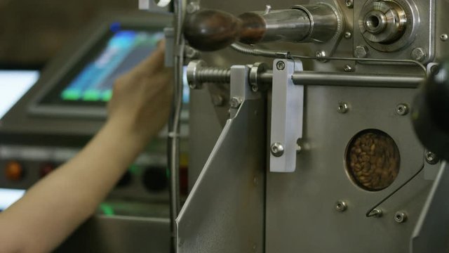 Coffee beans being roasted in a roastery as a person checks the temperature 