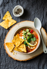 Vegetarian quinoa tomato soup with corn cheese chips, avocado and cilantro on grey background, top view