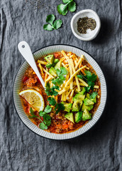 Crock pot vegetarian quinoa tomato soup with corn tortilla chips, avocado and cilantro on grey background, top view