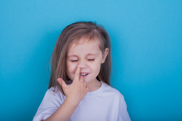 little girl with finger in his nose on blue background