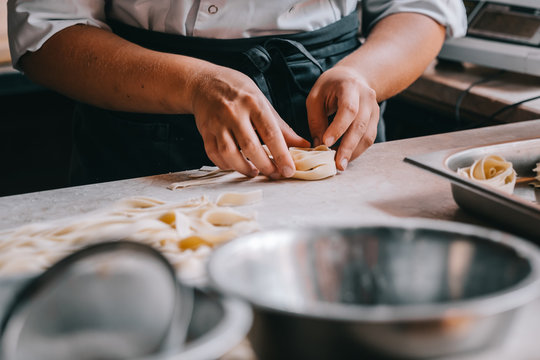 Chef woman's hands making tagliatelle pasta. Cooking process. Raw food photography concept.