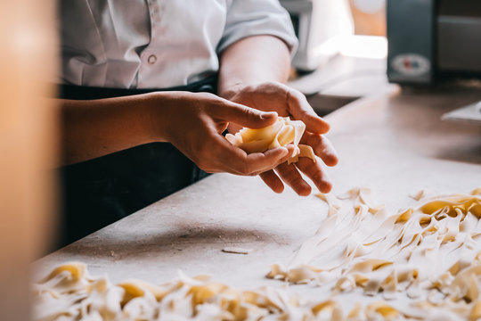 Chef woman's hands making tagliatelle pasta. Cooking process. Raw food photography concept.