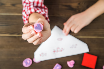 The girl writes a love letter for Valentine's Day. The girl writes a letter of thanks to mom and dad. Stamps and a letter on a textural wooden table. Diy love message