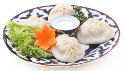 Uzbek manti with sour cream and herbs on a plate with an oriental ornament on a white background