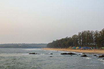 sea and rocks on the background of a sandy beach with green trees and colorful tents and resting people
