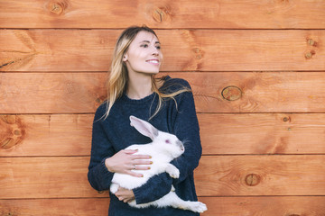 Young beautiful woman with a white rabbit in her arms next to a wooden house in the countryside