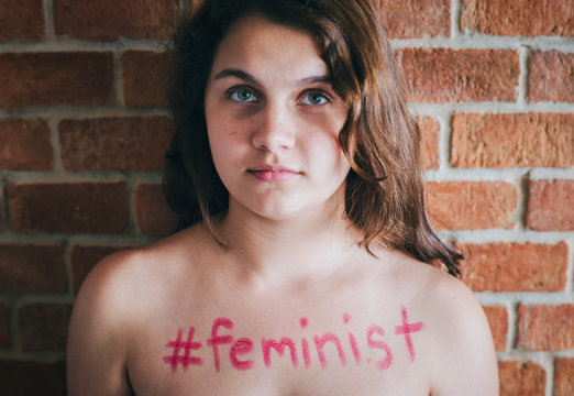 Girl with hashtag feminist written on her chest