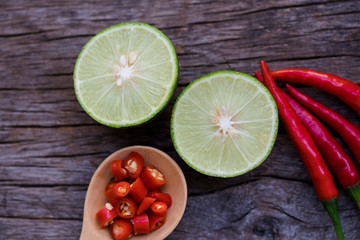 bowl of red chili peppers and green lime on the wooden background.