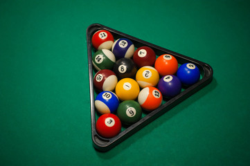 Sport billiard balls set arranged in shape of triangle on green billiard table in pub