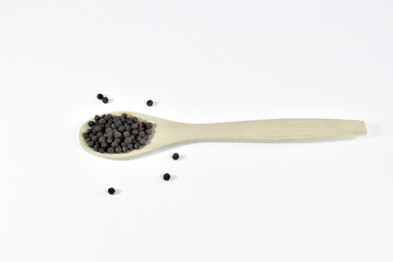 Black peppercorns close up,  in wooden spoon on a white background isolated