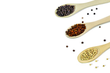 Black, red and white peppercorns close up,  in wooden spoons on a white background isolated