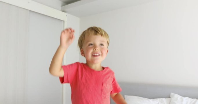 Happy kid raising his hands up imagining himself a tall adult.Boy reaching ceiling with arms up at home over a white background