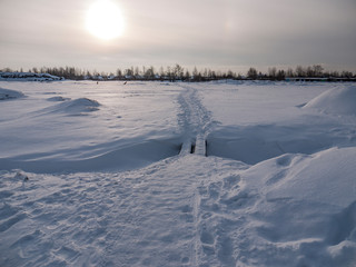 Fototapeta na wymiar Walkway with a bridge over a snowy field