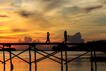 silhouette kids walk on the wooden jetty during sunset at Mantanani Island, Kota Belud, Sabah,...