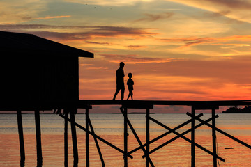 silhouette kids walk on the wooden jetty during sunset at Mantanani Island, Kota Belud, Sabah, Malaysia