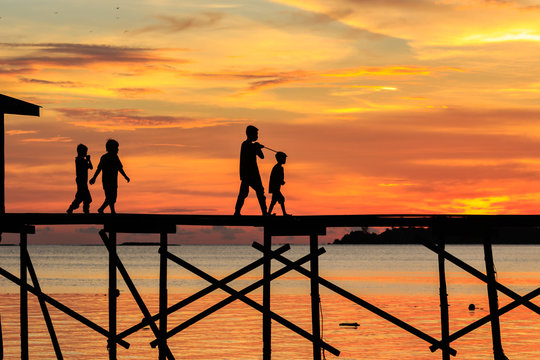 silhouette kids walk on the wooden jetty during sunset at Mantanani Island, Kota Belud, Sabah, Malaysia