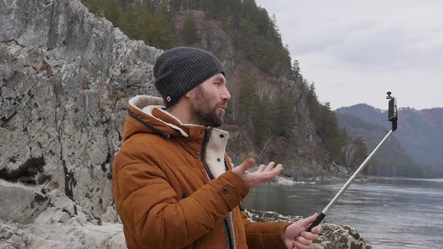 bearded tourist is broadcasting video on a mobile phone on the bank of a mountain river. slow motion
