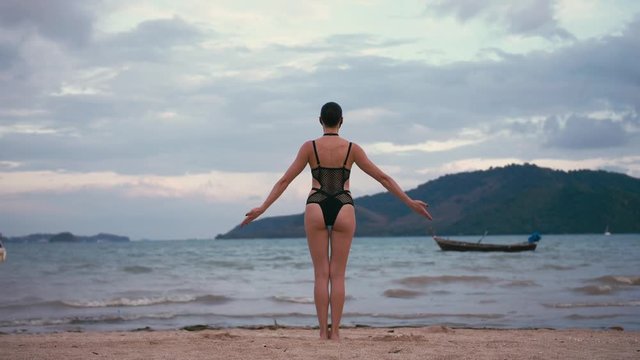 Caucasian woman practicing yoga at seashore wearing black swimsuit and medical anti-smog mask. Future concept