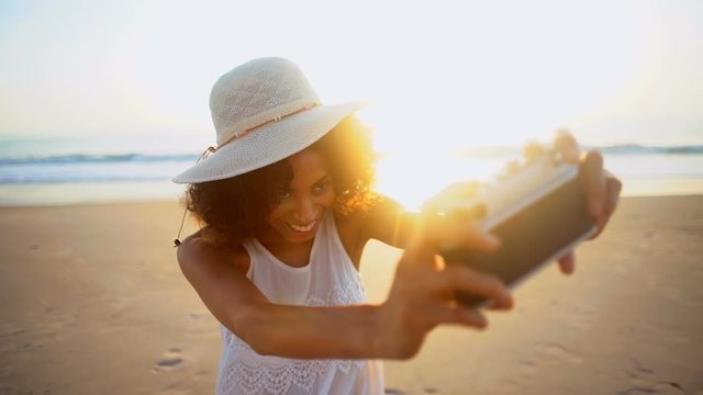 Young African American girl taking selfie on camera on holiday beach at sunset