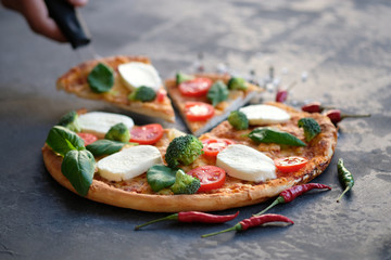 Sliced pizza with Mozzarella cheese, tomatoes, broccoli, Spices and fresh basil. Italian pizza. Pizza on black stone background