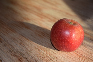Roter Apfel mit langen Schatten auf einem Holzbrett
