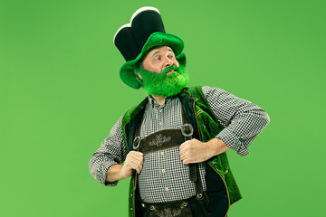 A smiling surprised happy senior man in a leprechaun hat with beard at green studio. He celebrates...