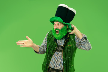 A smiling surprised happy senior man in a leprechaun hat with beard at green studio. He celebrates...