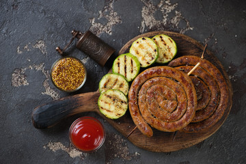 Rustic wooden serving board with bbq rolled sausages, zucchini and dipping sauces, studio shot on a...