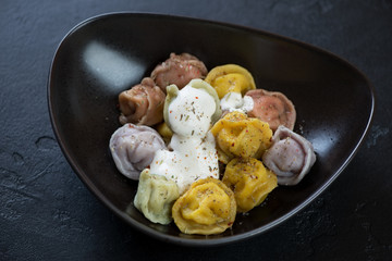 Boiled multicolored dumplings or pelmeni served in a black bowl, studio shot on a black stone background, close-up