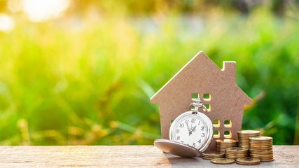 small house model and a clock with golden coins pile. - saving and investment for future planning...