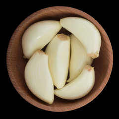 heap of shelled garlic in wooden cup isolated on black background. top view