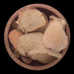 dried galangal in wooden cup isolated on black background. top view