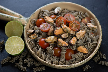 Hemp flour pasta with mussels and cherry tomatoes in a serving pan, studio shot, closeup
