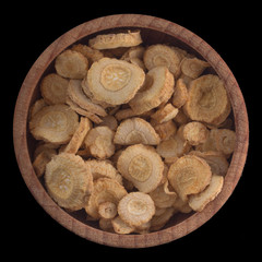 slices of root of parsley in wooden cup isolated on black background. top view