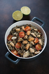 Fusilli made of hemp flour and served with tomatoes and mussels in a bowl, studio shot on a brown metal background
